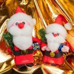 Two santa clause figurines sitting on a gold cloth.
