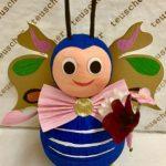 A blue bug with pink bow tie holding an umbrella.