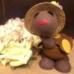 A brown teddy bear with a hat on next to some mushrooms.