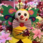 A colorful butterfly doll sitting in the middle of some flowers.