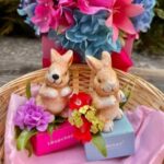 Two bunnies sitting in a basket with flowers.